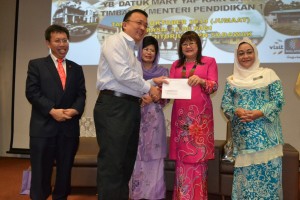 副教育部长叶娟呈颁发模拟支票予其中一间受惠学校代表蔡文铎，左一为人联党主席沈桂贤、左三为福利、妇女与家庭发展部长法蒂玛阿都拉，右一为教育局局长瑟琳娜。